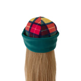A long blonde wig styled with a teal green fleece under-cap and a multicolor tartan plaid top, shown against a plain white background.