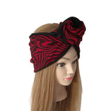 A red and black patterned fabric headwrap styled on a mannequin head with long blonde hair, set against a plain white background.