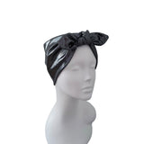 A black metallic headwrap turban with a large bow, displayed on a white mannequin head against a plain white background.