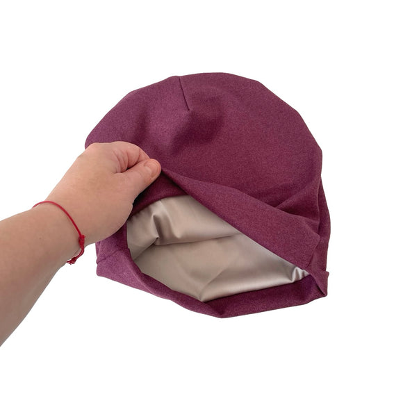 Purple fabric hat with beige interior held by a hand on a white background