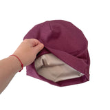 Purple fabric hat with beige interior held by a hand on a white background