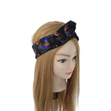 A black fabric headband with a Halloween spiderweb and pumpkin pattern, styled on a mannequin head with long blonde hair against a white background.