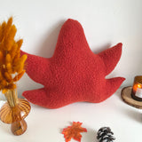 Red leaf-shaped pillow on a white surface with decorative elements.