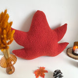 Red leaf-shaped pillow on a white surface with decorative elements.
