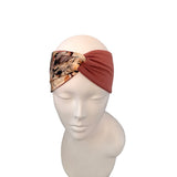 A twisted fabric headband displayed on a white mannequin head. The headband features a solid rust-red twisted knot and a matching patterned side panel with abstract floral-like designs in beige, brown, and black.