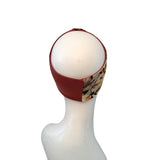 A fabric headband with a solid rust-red side and a camouflage print side, displayed on a white mannequin head against a white background.