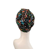 A multicolor floral turban hat with a black background, displayed on a white mannequin head against a white background.