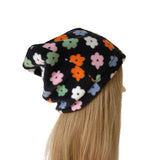 A black slouchy beanie hat with a colorful floral pattern, shown on a mannequin head with long blonde hair against a plain white background.