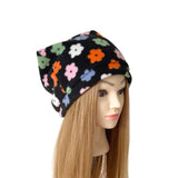 A black fleece slouchy beanie hat with a colorful floral pattern, displayed on a mannequin head with long blonde hair against a white background.