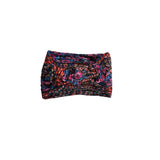 A multicolor knit headband with a twisted knot design, featuring a vibrant blend of pink, blue, orange, and black yarns, shown against a plain white background.
