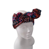 A multicolor floral knotted headwrap turban hat displayed on a white mannequin head against a plain white background.