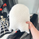 White ghost-shaped pillow held by a hand with Halloween decorations in the background