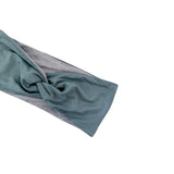 A twisted knot headband made of two-tone fabric, featuring a muted teal green outer layer and a heather gray inner layer, shown on a plain white background.