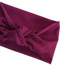 A close-up of a ribbed fabric headband in deep magenta, folded to show its texture and knot detail, set against a plain white background.