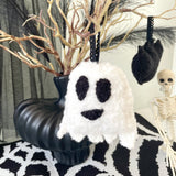 Decorative ghost ornament on a black and white patterned surface with Halloween decorations in the background.