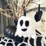 Decorative ghost ornament on a black and white patterned surface with Halloween decorations in the background.