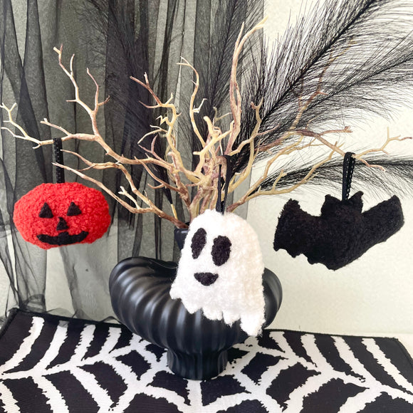 Halloween-themed decoration with a black pumpkin, white ghost, red jack-o'-lantern, and black bats on a patterned surface.