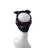 A black fabric headband with a Halloween-themed print of bats, spiderwebs, and orange pumpkins, displayed on a white mannequin head against a white background.