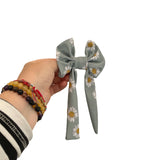 Hand holding a gray hair bow with white floral patterns on a white background