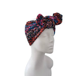 A multicolor floral patterned headwrap turban hat with a large bow on top, displayed on a white mannequin head against a solid white background.