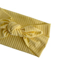 A close-up of a yellow ribbed fabric headband with a knotted bow, shown on a plain white background.