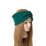 A dark green twisted fabric headband displayed on a mannequin head with long light brown hair, set against a plain white background.