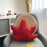 Red leaf-shaped pillow on a gray chair with a neutral background