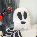 White ghost-shaped pillow with black eyes and mouth on a Halloween-themed background.