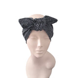 A black and gray leopard print headwrap turban with a large bow on the forehead, displayed on a beige mannequin head against a white background.