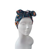 A multicolor floral and zebra-patterned fabric headwrap turban with a large bow, displayed on a white mannequin head against a solid white background.