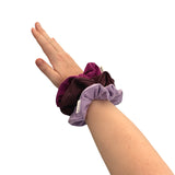 Hand wearing two purple scrunchies on a white background