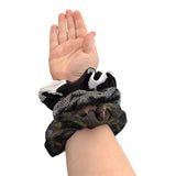 Hand wearing a black scrunchie with colorful patterns on a white background
