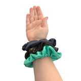 Hand wearing a turquoise scrunchie with feathers on a white background