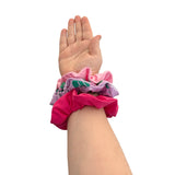 Hand wearing a bundle of colorful scrunchies on a white background