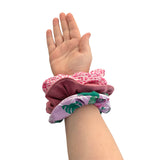 Hand wearing multiple colorful scrunchies on a white background