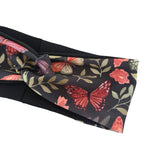A black fabric headband featuring a vibrant butterfly and floral print in red, pink, and green, styled with a knot on a plain white background.