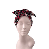A knotted headwrap or turban hat with a red, black, and beige leopard print pattern, displayed on a light gray female mannequin head against a plain white background.