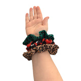 Hand wearing three patterned scrunchies on a white background