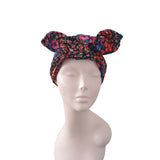 A multicolor floral headwrap turban hat with a bow, displayed on a light gray mannequin head against a white background.