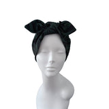 A black satin-like headwrap or turban with a large bow on top, displayed on a white mannequin head and shoulders against a plain white background.