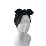 A black satin bow headwrap turban hat displayed on a white mannequin head against a plain white background.