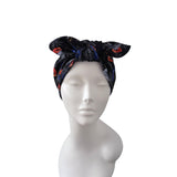 A black fabric headwrap turban with a red and blue floral pattern, displayed on a white mannequin head against a plain white background.