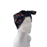 A black fabric headwrap or turban hat with a Halloween spiderweb and spider-themed print, displayed on a white mannequin head against a plain white background.