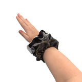 Hand wearing a black scrunchie with feathers on a white background