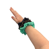 Hand wearing a green scrunchie with two additional scrunchies on a white background