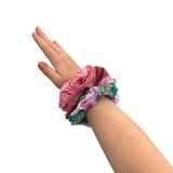 Hand wearing a stack of colorful scrunchies on a white background