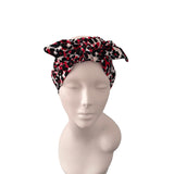 A patterned headwrap or headband displayed on a matte mannequin bust against a plain white background. The fabric has an abstract spotted pattern in red, black, and off-white.