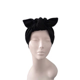 A black fabric headwrap turban with a large bow on top, displayed on a light gray mannequin head against a plain white background.