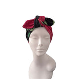 A red, black, and green patterned fabric headwrap styled on a white mannequin head against a plain white background.