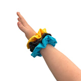 Hand wearing a blue scrunchie with yellow and black ones on a white background